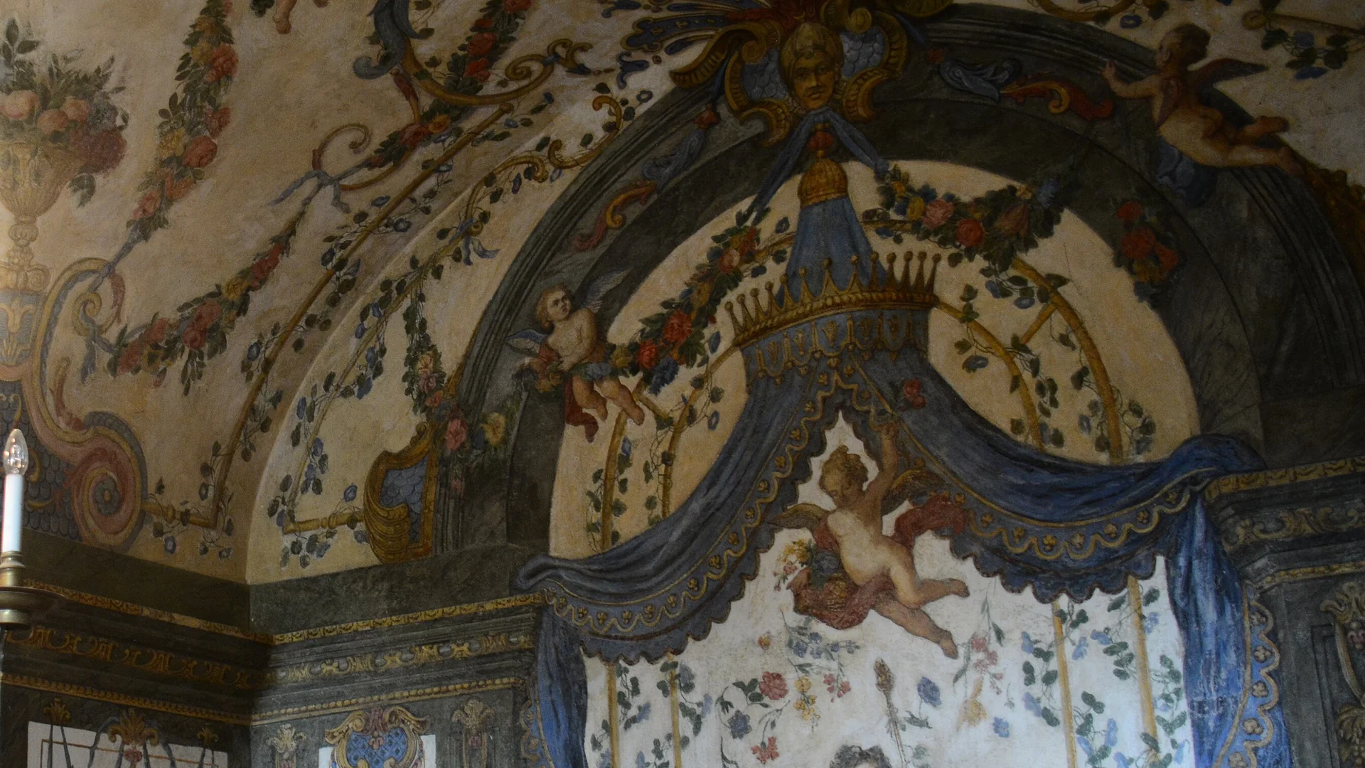 Wall and vault of the Sala Terrena in Vienna, painted with garlands, cherubs and a blue draped canopy with a gold crown over a scene on the wall.