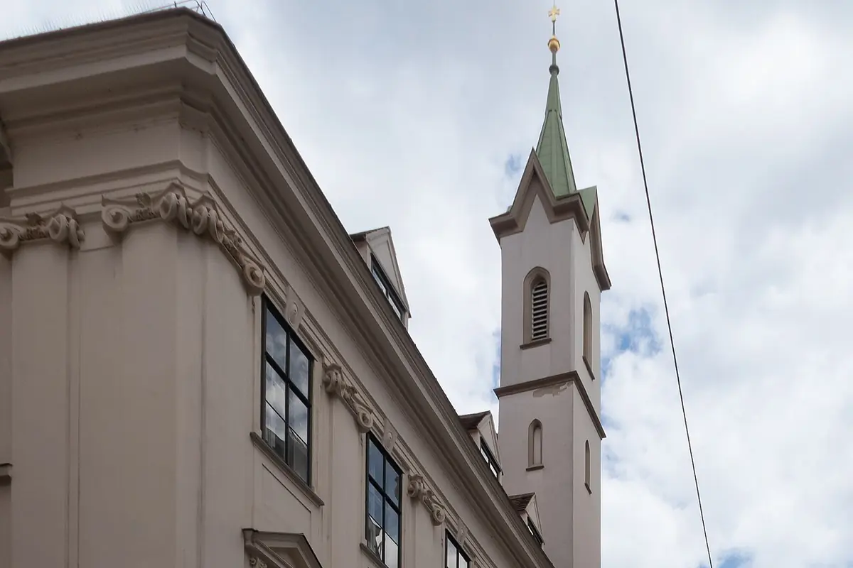 The Baroque corner of the Teutonic Order's house on Singerstraße in Vienna, with a slim church tower topped by a gold cross rising behind the roofline.