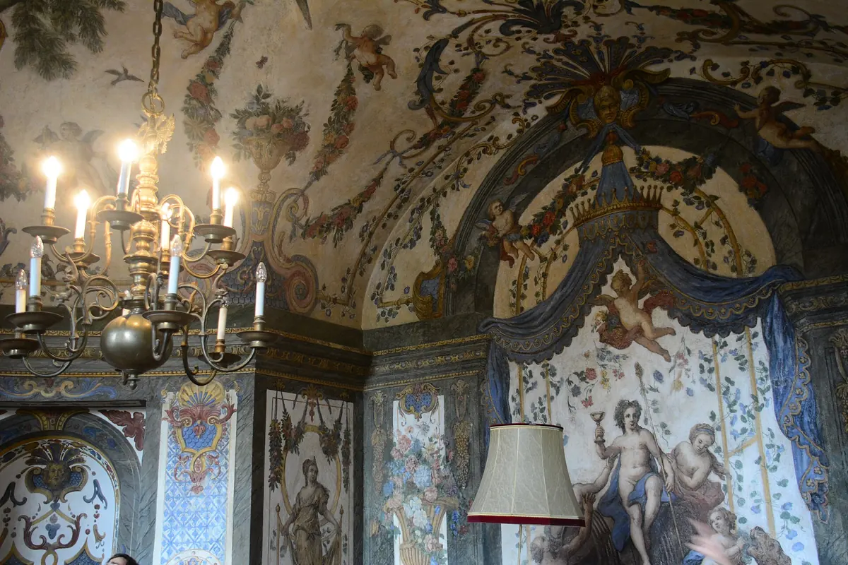 A corner of the Sala Terrena with a blue draped canopy painted over a mythological scene, garlands and cherubs on the vault and a brass chandelier.